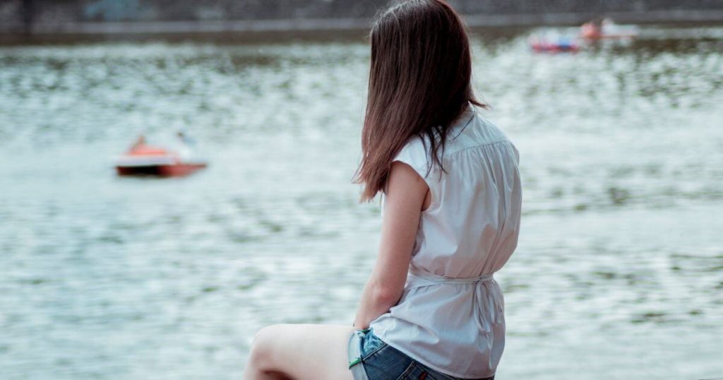寂しそうに湖の前で座っている女性
